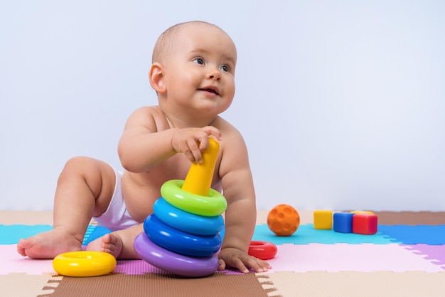 Un bambino gioca con una piramide di anelli multicolore. Sviluppo del pensiero e delle capacità motorie della mano