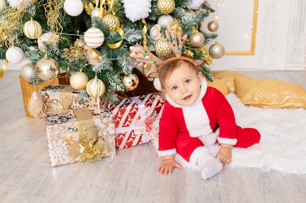 Un bambino in costume da Babbo Natale si siede all'albero di Natale con i regali, il concetto di nuovo anno e Natale