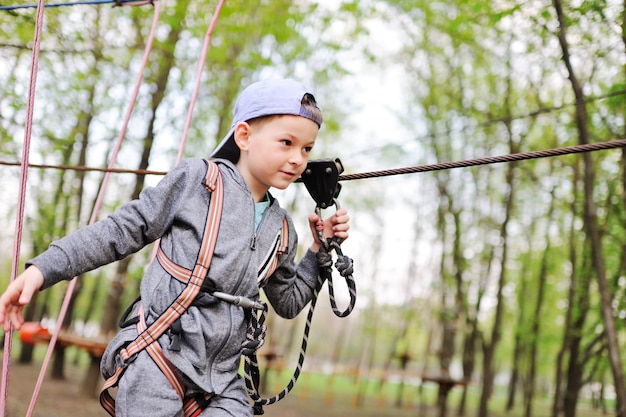 Un bambino in età prescolare ragazzo è un ostacolo in un parco di alta fune attrezzature alpinismo di sicurezza