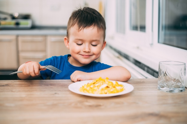 un bambino in maglietta in cucina che mangia una frittata, forchetta te stesso