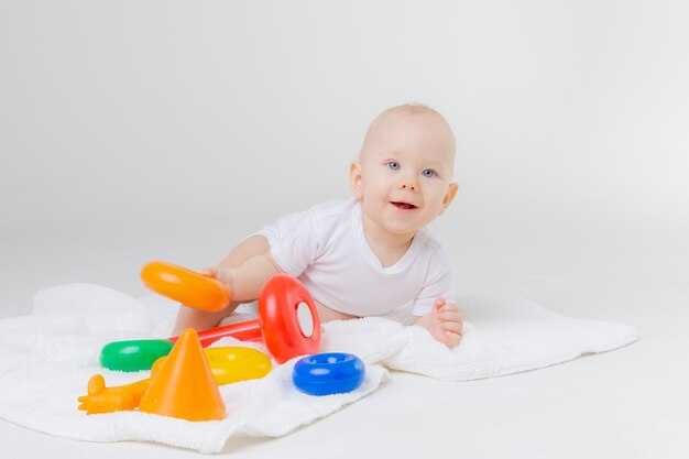 Un bambino in un body bianco sta giocando con una piramide multicolore su uno sfondo bianco seduto