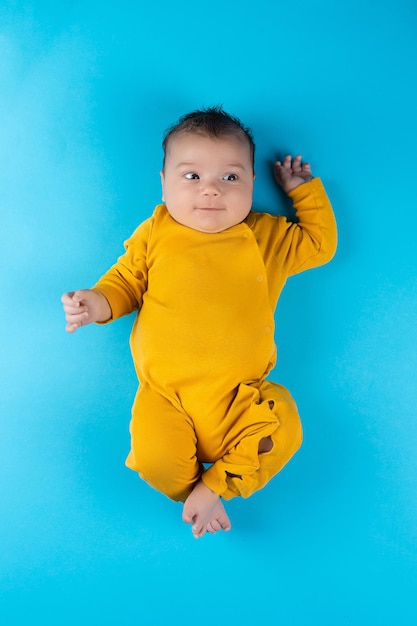 Un bambino in un body giallo giace su uno sfondo blu Divertente piccolo bambino Mockup per cartoline pubblicitarie per la celebrazione del design