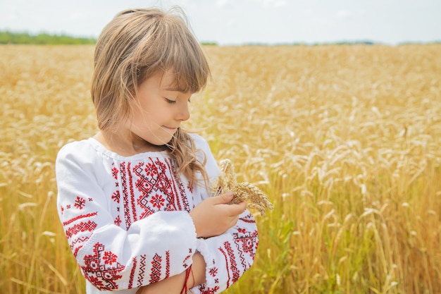 Un bambino in un campo di grano in una camicia ricamata.