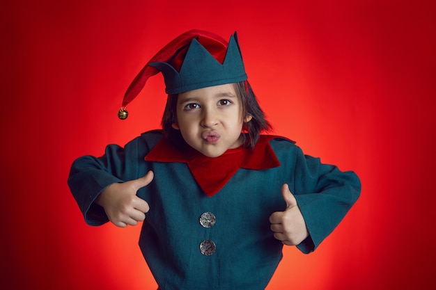 Un bambino in un costume da nano si trova su uno sfondo rosso il giorno di Natale