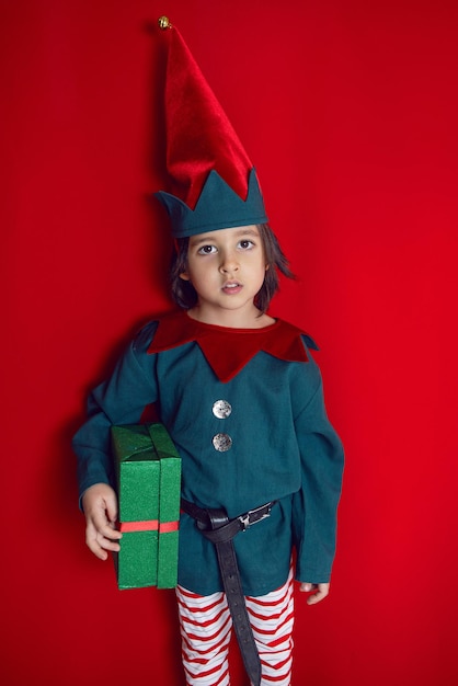 Un bambino in un costume da nano si trova su uno sfondo rosso il giorno di Natale