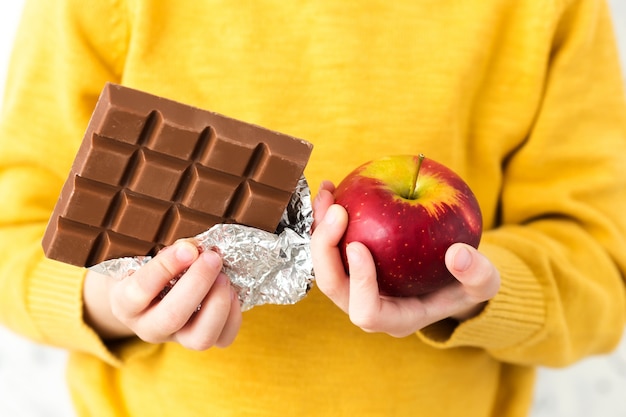 Un bambino in un maglione giallo in possesso di una mela e cioccolato.