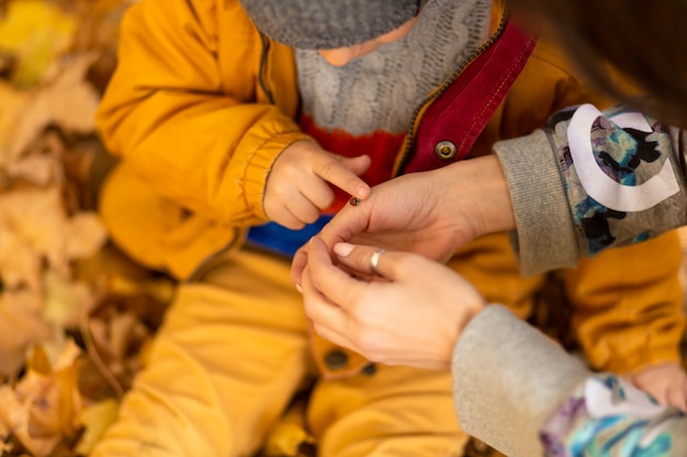 Un bambino in un parco in autunno si siede su foglie gialle in una giacca gialla e tiene una coccinella in mano ai bambini. Uno scarabeo rosso striscia sulle dita di un bambino.