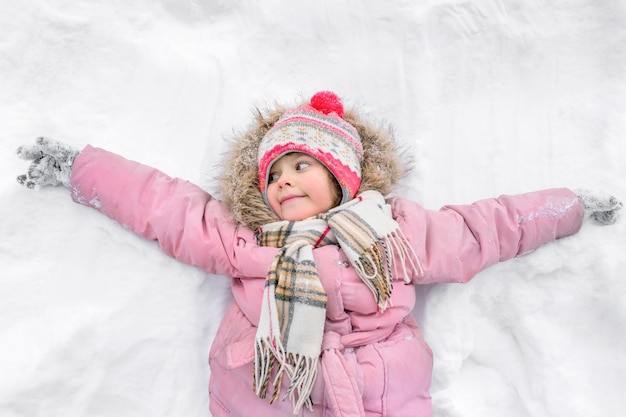 Un bambino in una giacca cappello sciarpa e guanti è sdraiato sulla neve all'aria aperta nel parco