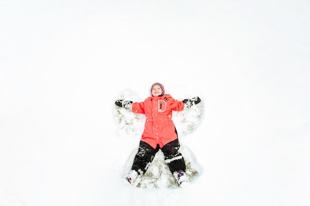 Un bambino in una tuta invernale rosa che si diverte, disteso sulla neve, con le braccia e le gambe divaricate.