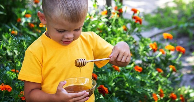 Un bambino mangia il miele in giardino da una ciotola trasparente della natura