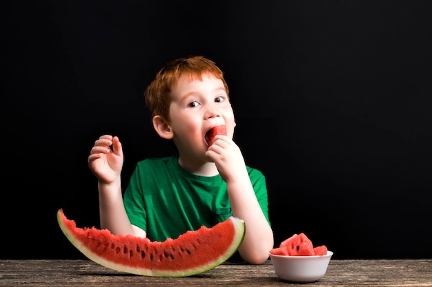 Un bambino morde le fette e mangia pezzi di anguria rossa succosa affettata sul tavolo, un prodotto alimentare naturale, primo piano di un'anguria rossa coltivata ecologicamente