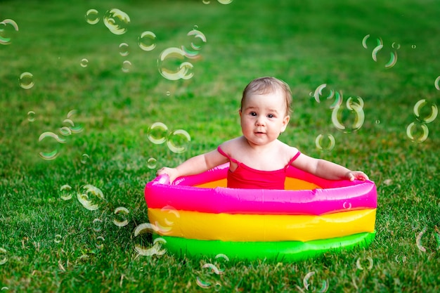 Un bambino nuota in una piscina gonfiabile in estate sull'erba verde con bolle di sapone, spazio per il testo