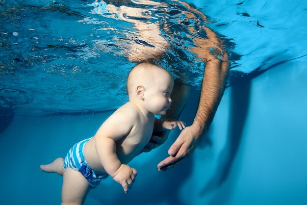 Un bambino nuota sott'acqua in piscina Papà mette le mani sott'acqua e prende il bambino