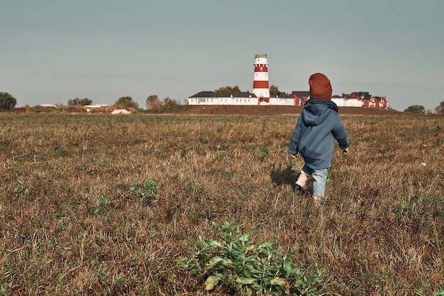 Un bambino piccolo cammina attraverso il campo sullo sfondo del faro, un bambino ha due anni. Autunno passeggiate nella natura.