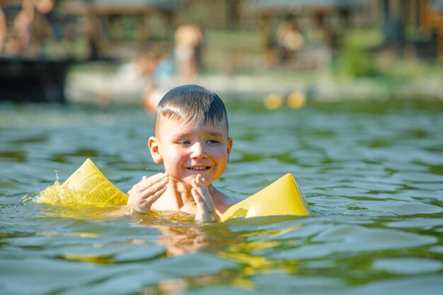 Un bambino piccolo che nuota nel lago con le braccia gonfiabili aiuta il supporto