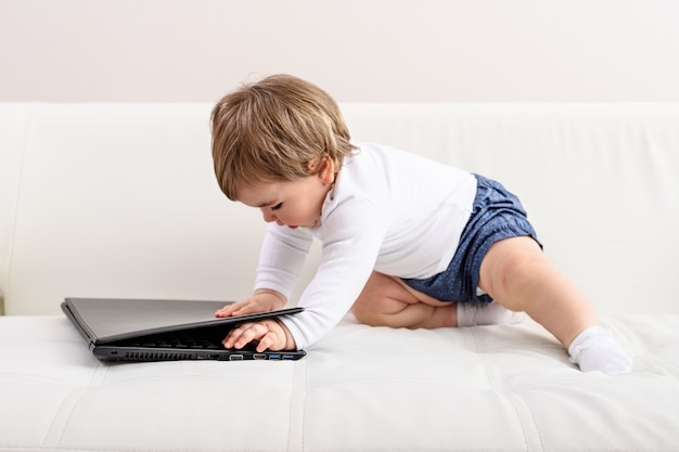 Un bambino piccolo con il computer portatile sul divano bianco, l'interesse dei bambini, piccolo capo