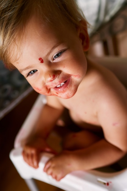 Un bambino piccolo con la faccia sporca si siede su una sedia girandosi di lato