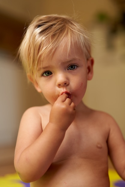 Un bambino piccolo con la faccia sporca tiene le dita in bocca