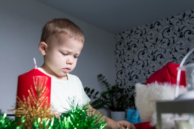 Un bambino piccolo con regali di Natale è seduto a un tavolo di legno di Capodanno con una tavoletta in mano