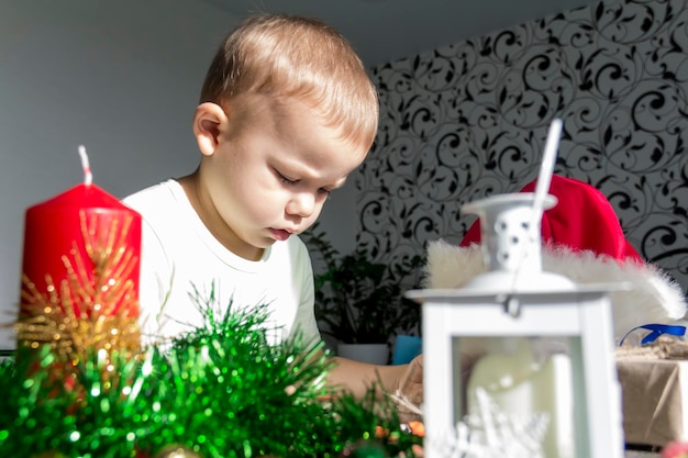 Un bambino piccolo con regali di Natale è seduto a un tavolo di legno di Capodanno con una tavoletta in mano