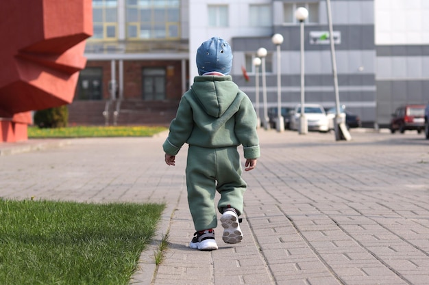 Un bambino piccolo con un vestito verde e scarpe da ginnastica cammina nel parco