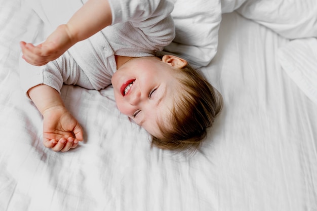 Un bambino piccolo da vicino sdraiato su un lenzuolo bianco in una stanza luminosa a casa