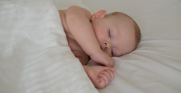 Un bambino piccolo dorme sotto una coperta bianca.