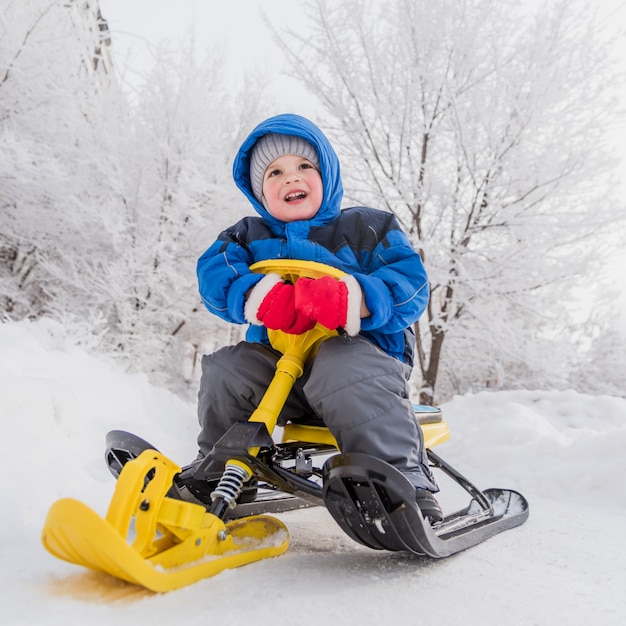 Un bambino piccolo è seduto su uno scooter da neve in inverno