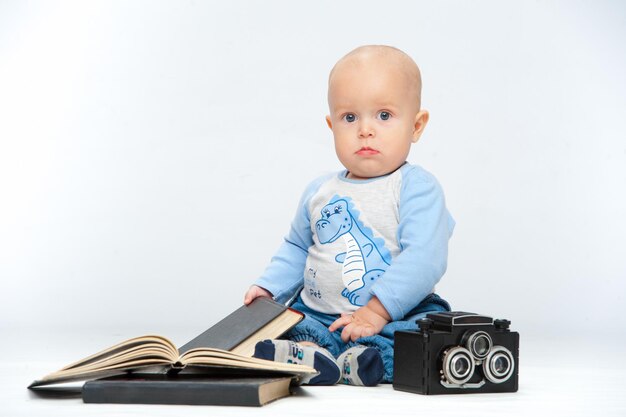 Un bambino piccolo e una macchina fotografica su uno sfondo bianco neutro.