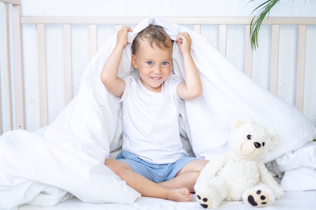 Un bambino piccolo giace in una culla con un orsacchiotto su biancheria da letto bianca un sorriso da sogno di un bambino