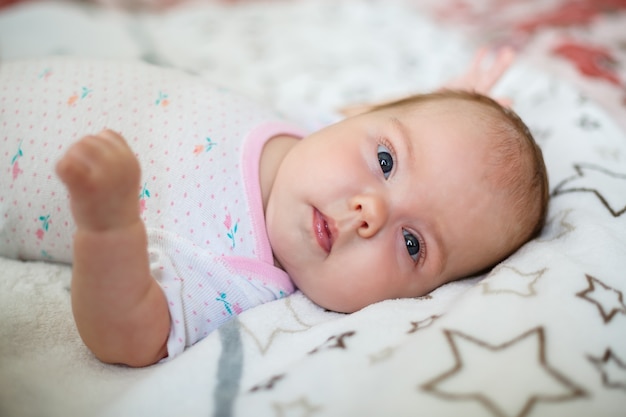 Un bambino piccolo giace su un lenzuolo bianco. Vestiti per bambini che giacciono nella culla