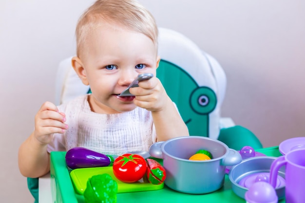 Un bambino piccolo gioca ai piatti dei bambini con le verdure seduto a tavola