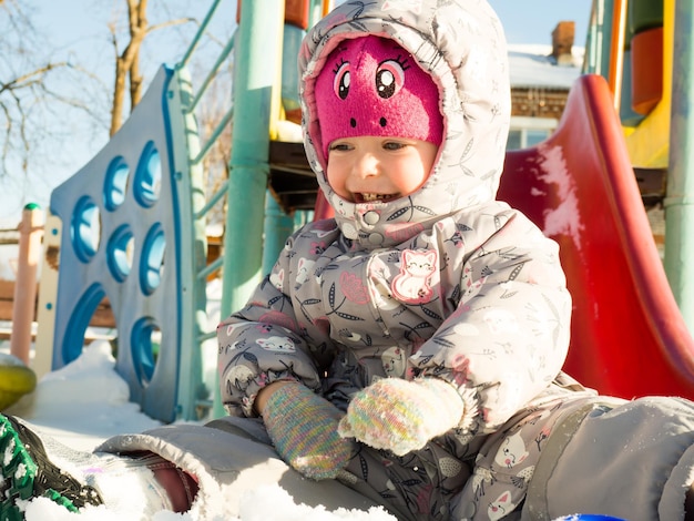 Un bambino piccolo gioca nel parco giochi con la neve.