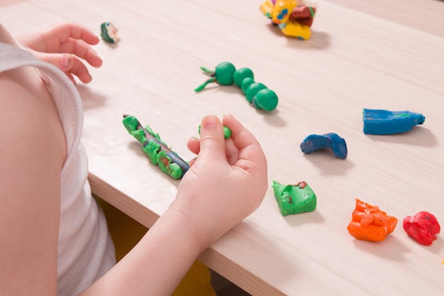 Un bambino piccolo scolpisce dalla plastilina su un tavolo di legno