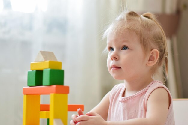 Un bambino piccolo sta giocando a un tavolo con un kit di costruzione in legno Un gioco con i cubi Giochi per bambini