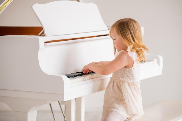 Un bambino piccolo suona un grande pianoforte bianco in una luminosa stanza soleggiata