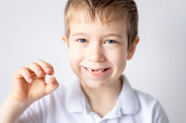 Un bambino piccolo tiene in mano il suo primo dente da latte caduto Il bambino cresce i denti cadono Cura dei denti da latte e della cavità orale