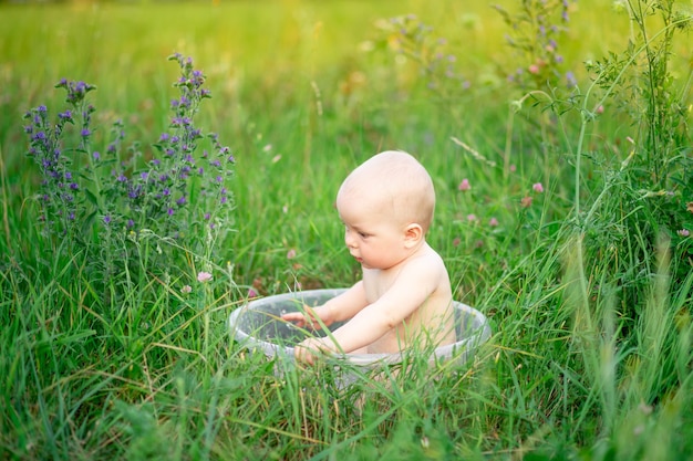 un bambino piccolo una bambina di sei mesi fa il bagno in una bacinella di schiuma su un prato verde d'estate