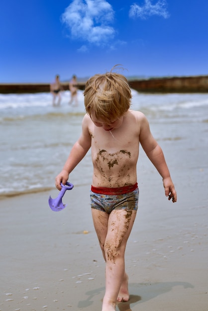 Un bambino si sporca nel fango e cammina piangendo lungo la spiaggia lungo il mare