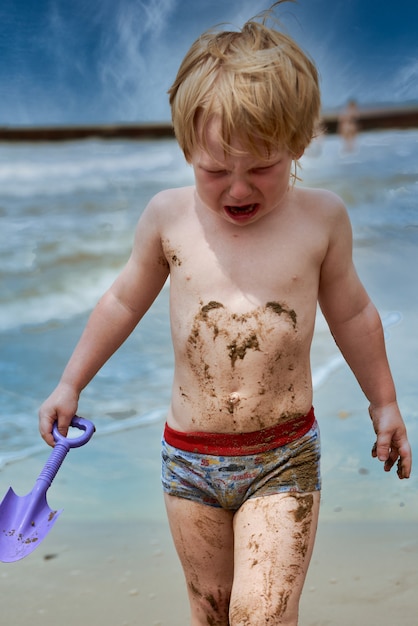 Un bambino si sporca nel fango e cammina piangendo lungo la spiaggia