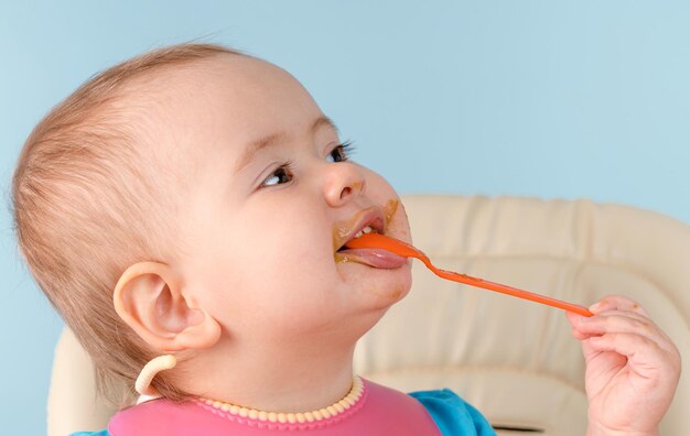 Un bambino sorridente felice di 1217 mesi mangia la purea di verdure dei broccoli con un cucchiaio