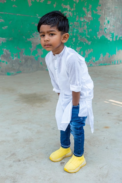 Un bambino sorridente posa per una foto indossando Punjabi bianco e blue jeans con una scarpa gialla come abito moderno Un bambino di due anni guarda lontano con una faccia curiosa