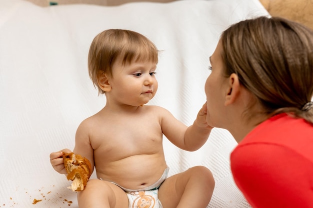 Un bambino sta mangiando un panino con una donna con una camicia rossa.