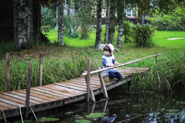 Un bambino sta pescando in autunno mattina Tramonto autunnale sullo stagno Un pescatore con una canna da pesca sulla passerella