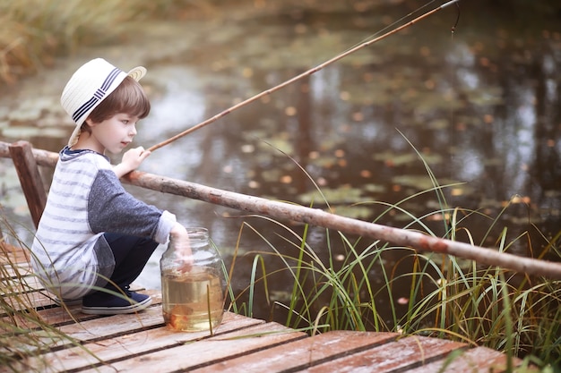 Un bambino sta pescando la mattina d'autunno. Tramonto autunnale sullo stagno. Un pescatore con una canna da pesca sulla passerella.