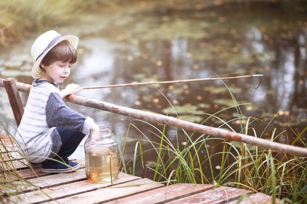 Un bambino sta pescando la mattina d'autunno. Tramonto autunnale sullo stagno. Un pescatore con una canna da pesca sulla passerella.