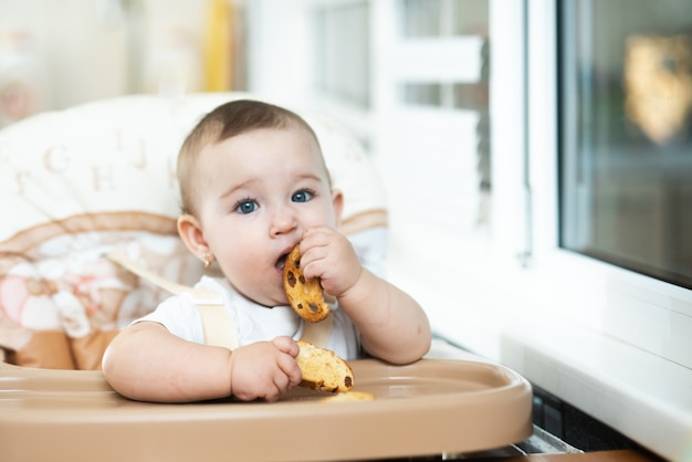 Un bambino su un seggiolone che mangia un cracker con uvetta