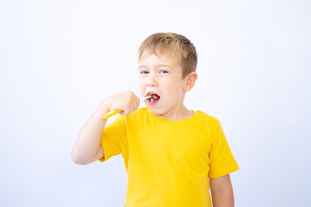 un bambino su uno sfondo bianco si sta lavando i denti tenendo in mano uno spazzolino da denti isolare
