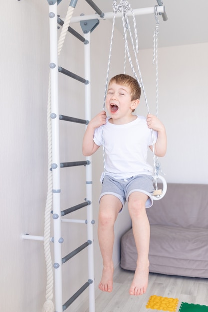 Un bambino sul muro svedese fa sport a casa, un ragazzo sale una scala con una corda, il concetto di sport e salute