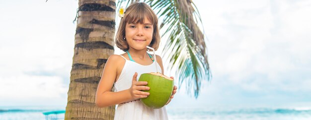 Un bambino sulla spiaggia beve cocco